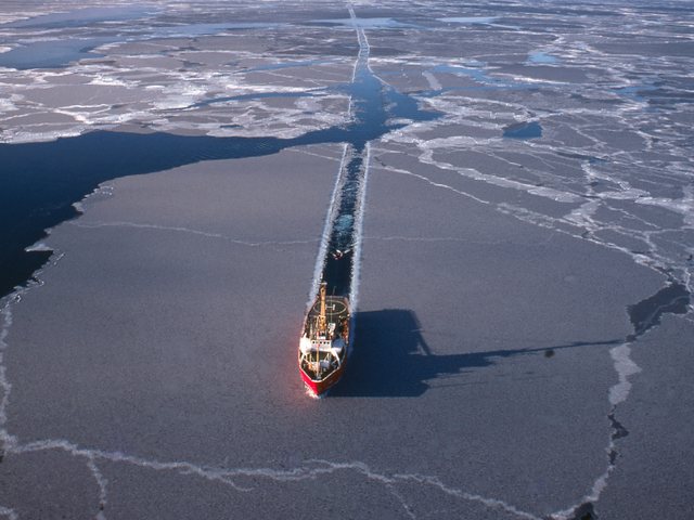 A research vessel cutting a channel through Arctic sea ice, seen from above.